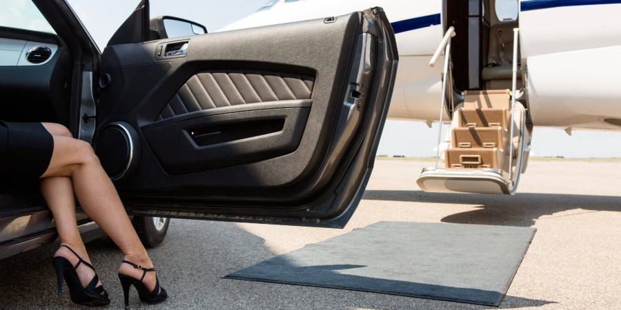 luxury high taxpayer woman in black heels getting out of black luxury car in front of private jet and red / grey carpet.