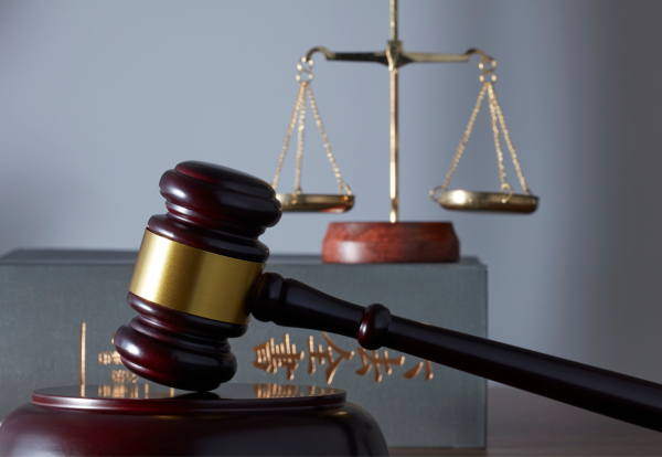 A top-down photograph of a person in a white shirt working on a silver and black laptop on a dark, wood-grain desk. To the left of the laptop are several black and white office supplies, including a black spiral notebook, a white wallet, a desk organizer with a pencil, paper clips, and sticky notes, and a partially visible tablet or phone at the bottom. A white cup of coffee is near the top right. Property Tax Advice Expat Tax Advice PTA ETA Riverview Portfolio