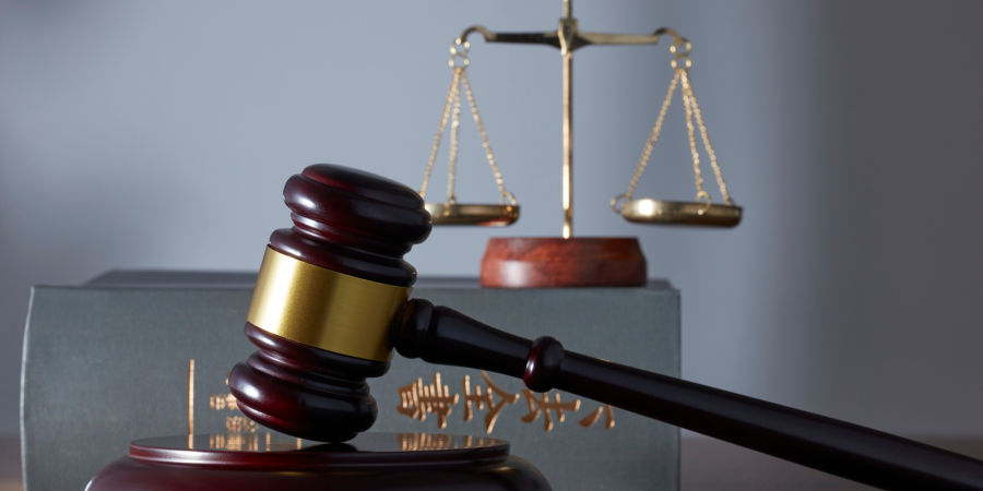 A top-down photograph of a person in a white shirt working on a silver and black laptop on a dark, wood-grain desk. To the left of the laptop are several black and white office supplies, including a black spiral notebook, a white wallet, a desk organizer with a pencil, paper clips, and sticky notes, and a partially visible tablet or phone at the bottom. A white cup of coffee is near the top right. Property Tax Advice Expat Tax Advice PTA ETA Riverview Portfolio